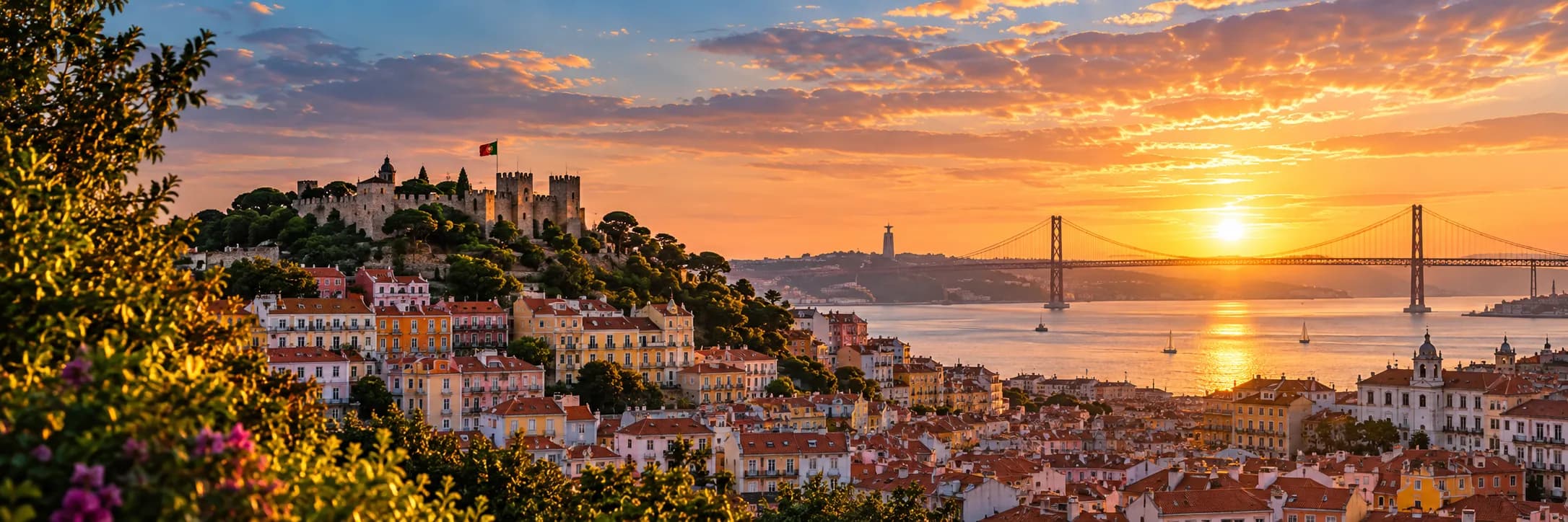 Lisbon at sunset from a hilltop viewpoint, with Sao Jorge castle and the Portuguese flag on the left and the Tagus and the 25 de Abril bridge on the right.