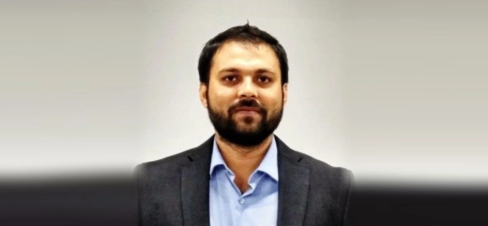 Portrait of Abhijeet Singh in a dark blazer and light blue shirt against a plain grey background.