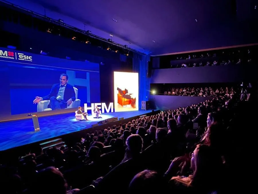 A full auditorium facing a stage with the HEM letters and a speaker on the big screen, at a previous edition of Hoy Es Marketing.